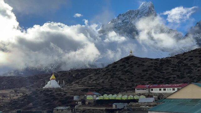 Life in Dingboche village in Everest region, Nepal. Trekkers walking through Himalayan landscape with stupas, guesthouses and moving clouds over snowy mountains