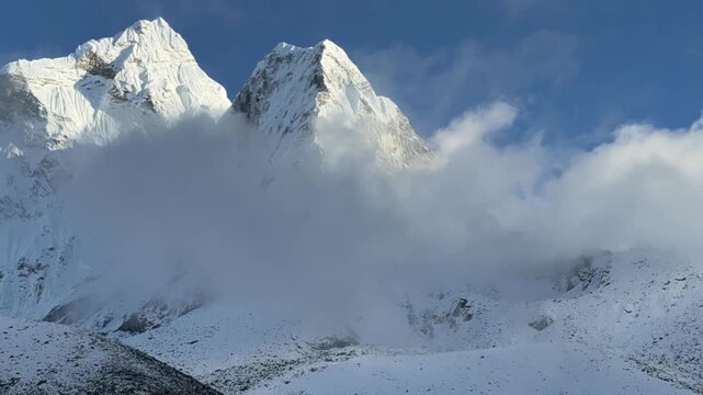 Fast moving clouds around high snow-covered mountain peak in Everest region, Nepal. Timelapse effect, dramatic Himalayan landscape, blue sky and mist