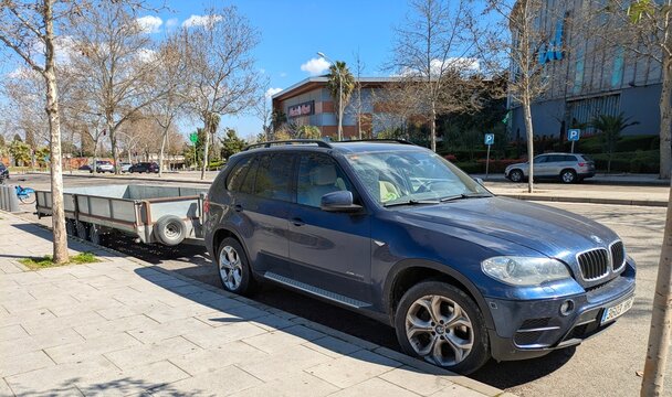 Autom&oacute;vil BMW X5 con remolque abierto para carga general, aparcado en una calle de Madrid, Espa&ntilde;a, 13 de marzo de 2026