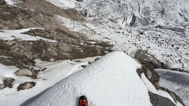 Point of view shot of feet standing on the edge of a snowy cliff in the Himalayas, then camera reveals a deep gorge with ice formations and high mountain peaks on the Everest Base Camp trail