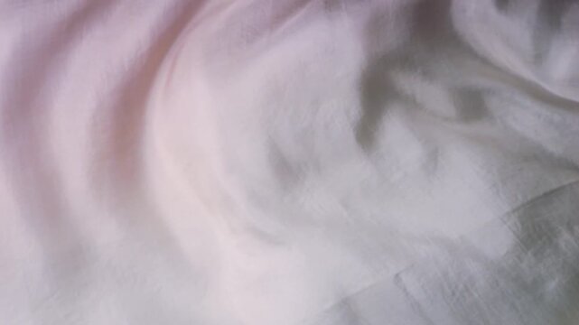 Natural silk fabric fluttering in the wind. Abstract wave background with soft shadows. Light pink color with smooth surface. Organic texture of real natural silk.