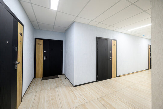 modern hallway with light beige tiled flooring, light grey textured walls, black doors with wooden panels, numbered 445&ndash;447, recessed ceiling lights, clean and minimalistic design