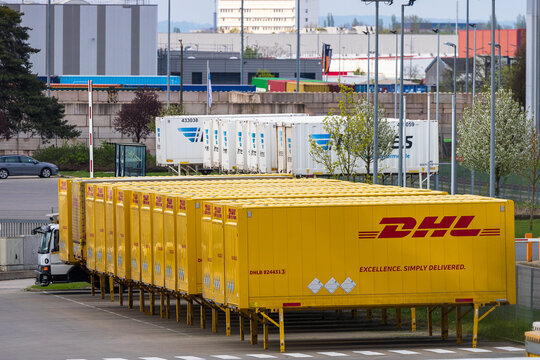 Mehrere gelbe Wechselbr&uuml;cken mit DHL-Logo und Aufschrift &bdquo;Excellence. Simply Delivered." stehen aufgereiht auf einem Logistikgel&auml;nde.