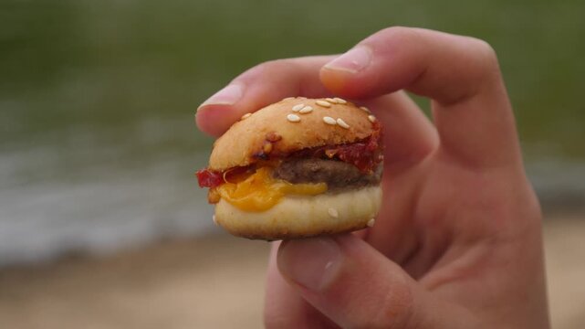 Closeup holding a small tasty burger with fingers showing its layers from side