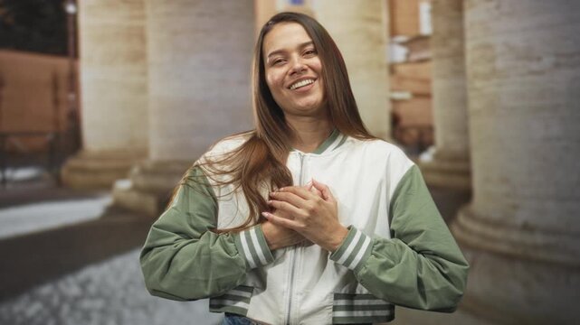 Woman smiling with hands clasped over chest in front of stone colonnade building; gratitude warmth trust.