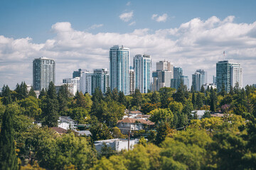 Fototapeta premium Modern city skyline with high rise buildings and lush green trees under partly cloudy sky, showcasing urban and natural contrast in peaceful atmosphere