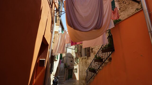Rovinj, Croatia - August 14, 2025: Linen sheets and colorful laundry hang on lines strung between narrow, sun-drenched alley walls of an old Mediterranean town under a clear blue sky.