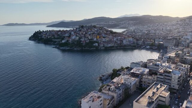 Drone footage of a dense coastal peninsula neighborhood over calm bay water with evening light.