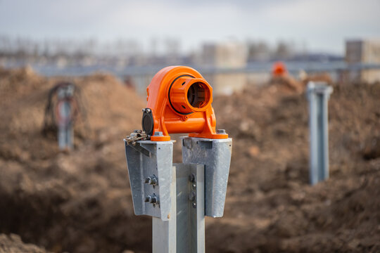 Orange construction mounting bracket on galvanized metal post in rough earthwork field with blurred site hardware for solar infrastructure project