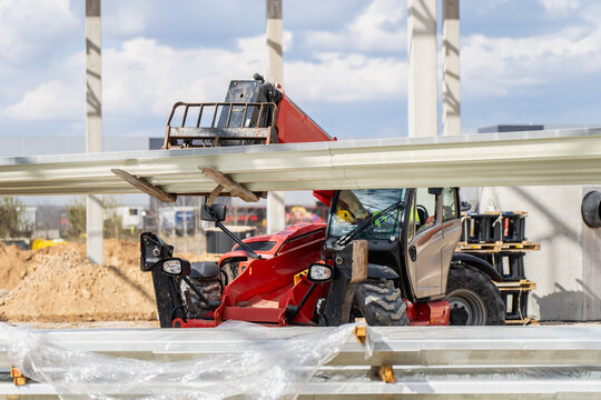Heavy telescopic handler moving long cladding panels through warehouse frame construction site for material handling and structural assembly tasks