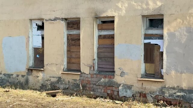 Boarded ground floor windows abandoned apartment. Cracked plaster and exposed brick around boarded openings, flaking paint.