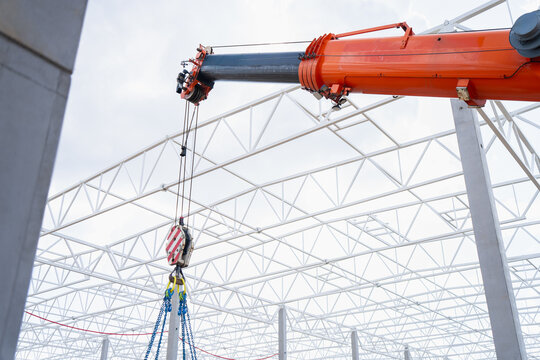 Mobile crane lifting rig suspended below orange telescopic boom inside white steel truss frame for warehouse construction load handling tasks