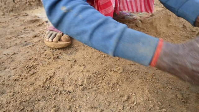 A person manually shaping bricks in an open field. Using a rectangular wooden mold and raw, reddish-brown clay, the worker skillfully forms each brick on the dusty ground. Slow motion video.