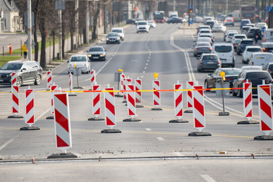 Urban roadworks with red white traffic delineators blocking multiple lanes on busy city street during street reconstruction and traffic management