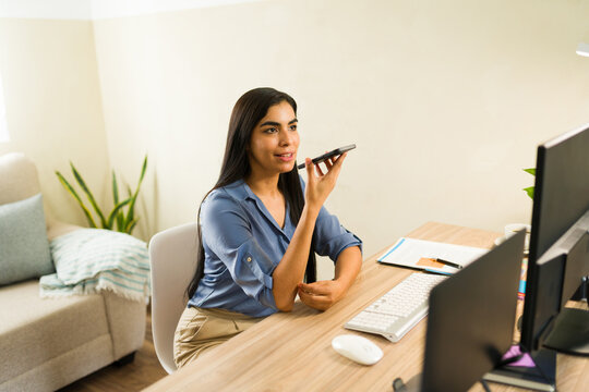 Professional woman using phone on speaker while working at desk, communicating with colleagues or clients