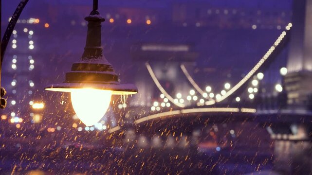 Budapest, Hungary - January 6, 2026: A glowing street lamp covered in snow and icicles shines brightly against the bokeh of the Chain Bridge during a winter evening in Budapest.