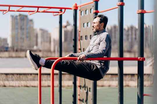 Man doing L sit exercise on parallel bars outdoors