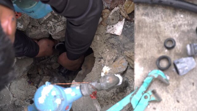 Professional plumber hands fixing a broken water pipe inside a hole in concrete. Background shows plumbing tools, pipe fittings, and a blue water meter. Maintenance and repair service concept.