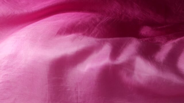 Soft pink silk fabric develops smoothly in the wind. Natural silk material creates abstract waves on the background. Flowing texture of the plain pink textile moves in slow motion.