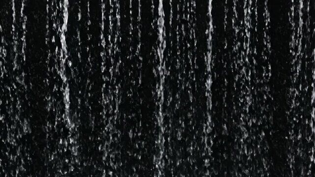 Water droplets falling vertically against a black background. Abstract texture of rain curtain or fountain spray.