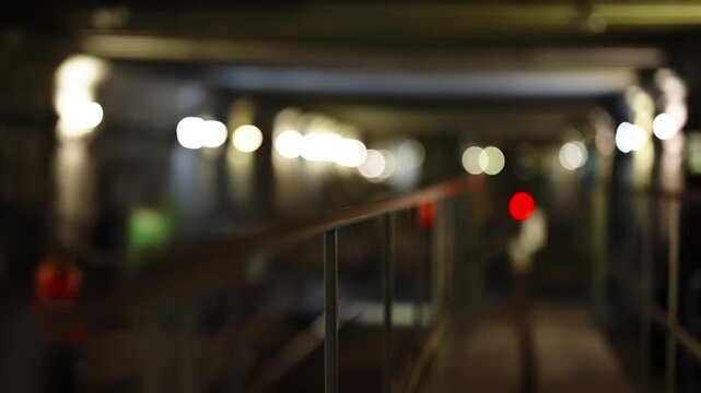 Abstract blurred urban walkway with metal railing and glowing bokeh lights in a dimly lit tunnel, conveying depth and perspective, with a distant red signal providing contrast