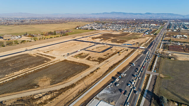 Aerial View of Large New Residential Development Under Construction Along Busy Highway with Mountain Range Backdrop