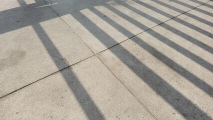 Fototapeta premium Geometric shadows on the concrete floor. Abstract composition of grid-like shadows on a concrete surface. Natural light creating striking geometric lines and patterns.