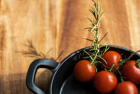 Culinary still life of juicy red tomatoes in a black pan and garlic cloves on a dark textured surface