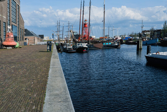 Wide angle view of historic sailing ships and a red lighthouse boat moored at a harbor quay under a cloudy sky in Den Helder, Netherlands