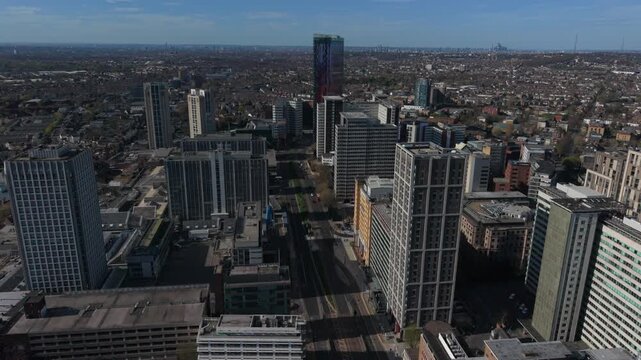 Flying between Croydon skyscrapers in city center.  Aerial view above the street with light traffic. Modern architecture of high rise buildings. View towards London skyline on a sunny day.
