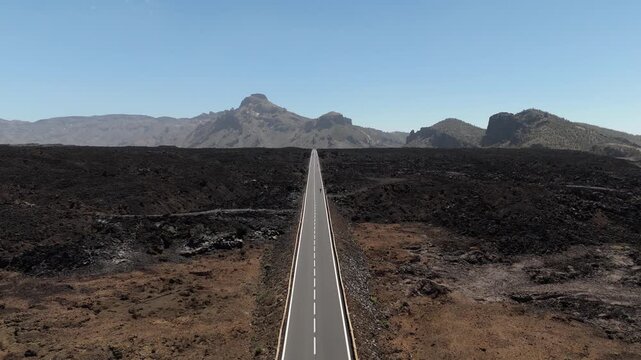 Aerial view from a drone flying over a road among a lava field with mountains in the background in Teide National Park on Tenerife