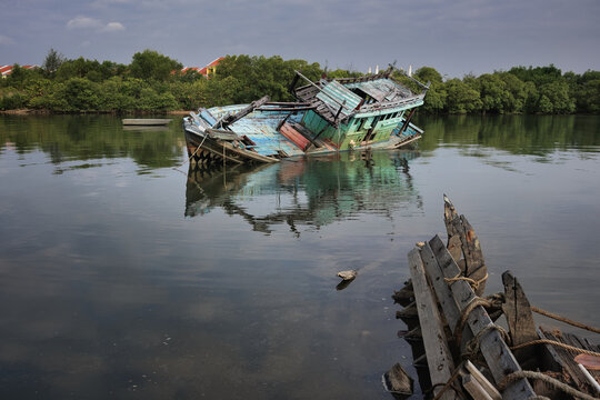 Shark mouth fishing boat half sinking in Marang River, Terengganu under cloudy sky