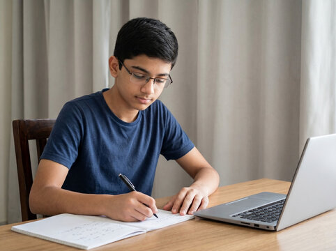 indian teenage boy studying at desk with notebook and laptop preparing for competitive exams like jee, neet, cat, gmat, cmat and board exams
