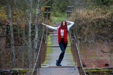 Naklejka premium Young Woman in Red Scarf Posing on Old Wooden Bridge in Autumn