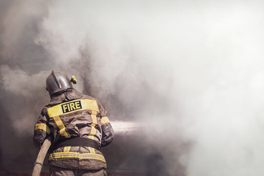 Firefighter spraying water on burning building with smoke and copy space