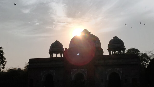 Silhouette of Humayun's Tomb at sunset with bright sun flare and flying birds