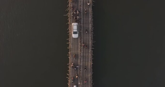 Top down aerial view at nightfall of cars and motorbikes crossing a long bamboo bridge over water 
