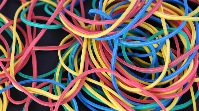 A chaotic tangle of vibrant multicolored elastic rubber bands scattered over a dark surface. Close up.
