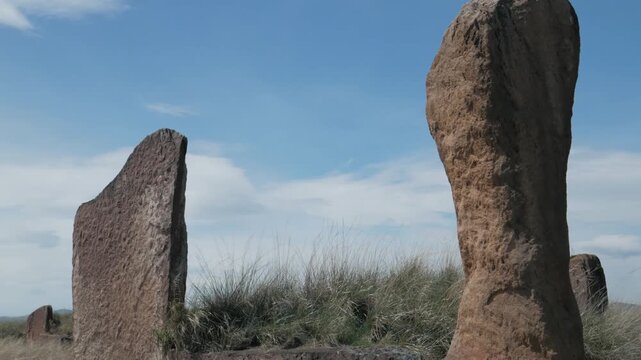 Handheld static close-up of massive ancient standing stones at Great Salbyk Kurgan, Khakassia. Weathered megaliths stand tall against a blue sky with light clouds in the Valley of Kings.