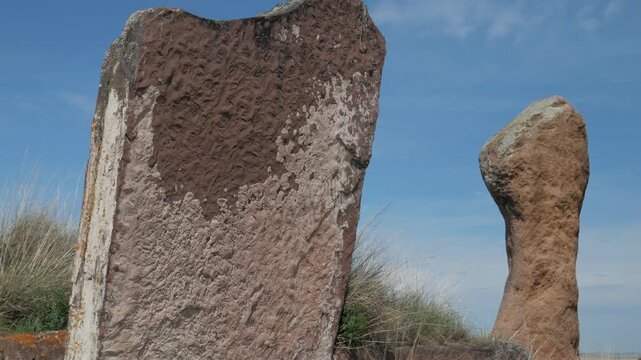 Handheld static close-up of highly textured ancient standing stones at Great Salbyk Kurgan, Khakassia. Focus on the detailed, rough, eroded surface of the megalith against a clear blue sky.