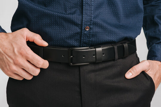 Close-up of a man wearing a black leather belt with a black buckle on dark trousers and a blue patterned shirt.