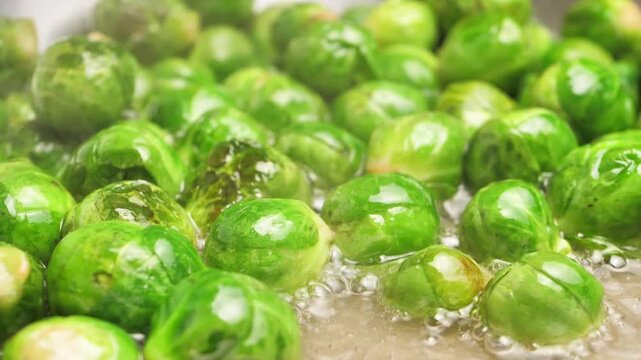 Many green sprouts of Brussels sprouts frying in a frying pan with a large amount of oil releasing steam. Frying fresh sprouts of Brussels sprouts in hot oil. Vegetarian plant based hot food.