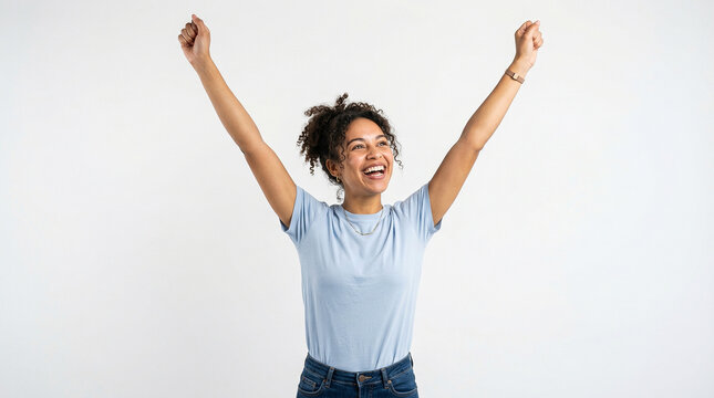Photograph of a joyful woman with dark skin, short curly hair, wearing a light blue t-shirt and jeans, raising her arms triumphantly against a plain white background.