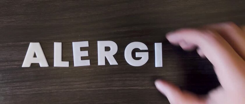 persona escribiendo la palabra alergias en un fondo oscuro con letras blancas y pre hechas
