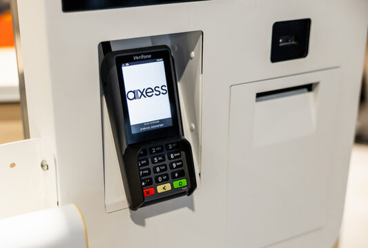 close-up of payment Verifone P400 Plus terminal mounted on a wall. The terminal displays a logo Axess and has a keypad with various buttons for transactions. The kiosk is modern and sleek in design.