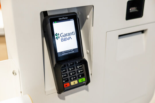A close-up of a payment terminal attached to a machine, displaying the logo of Garanti BBVA. The terminal features a keypad with colorful buttons.