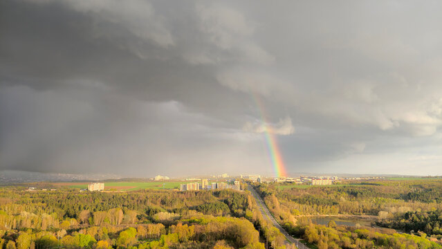 Rainbow appearing over city, forest, and storm clouds
