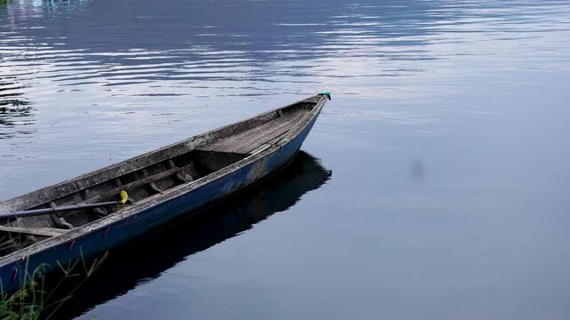 Old weathered wooden canoe moored on the calm waters of Selorejo Reservoir, Indonesia, featuring ample negative space on the right for text or design copy.
