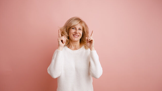 Adult woman smiling, enthusiastically pointing both index fingers upwards, suggesting ideas or information in a studio setup