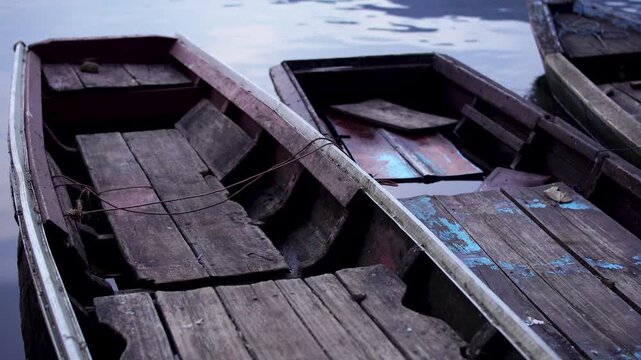 Close up top view focusing on the leftmost of three weathered wooden fishing boats bobbing together at Selorejo Reservoir, Malang, Indonesia, showing rural daily livelihood and decay.